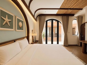 A hotel room with a large bed, a starfish and seashell artwork on the wall, a balcony with curtains, and a wooden ceiling.