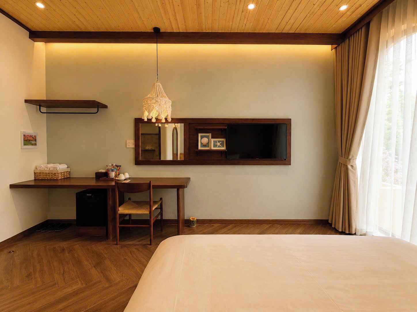 Une chambre d’hôtel avec un plafond en bois, un lit, un bureau avec une chaise, un miroir et une fenêtre avec des rideaux.