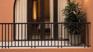 Fachada de edificio con un balcón, una planta en maceta y una lámpara de pared encendida.