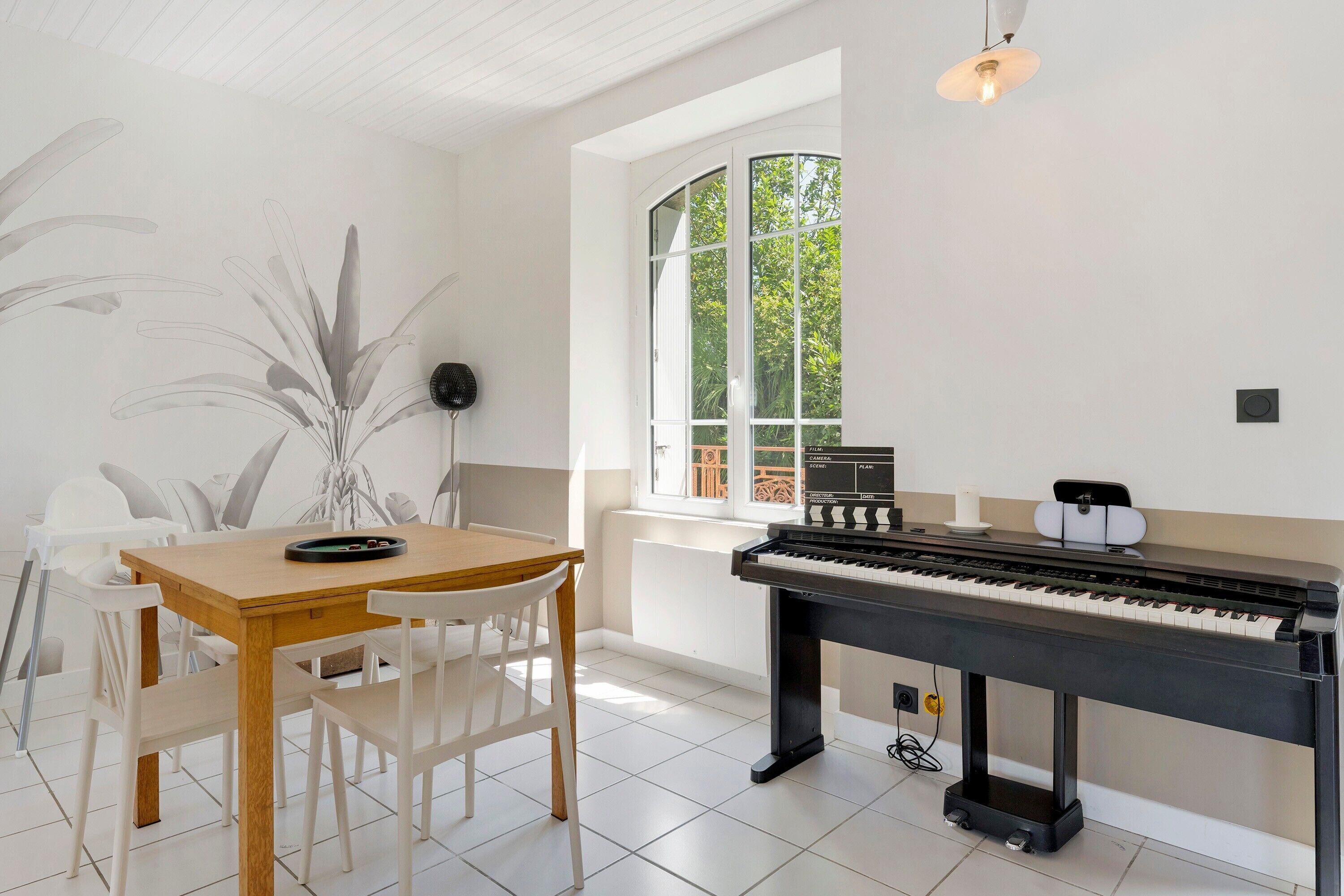 A piano, a dining table with chairs, a large window, and a ceiling fan.