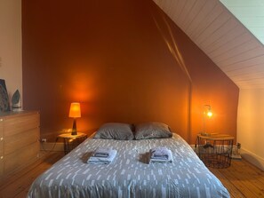 Una camera da letto con soffitto spiovente, un letto con copripiumino decorato, due abat-jour e un piccolo tavolo con lampada.