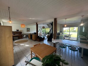 Uma sala de estar ampla com uma mesa de jantar de madeira, cadeiras, área de cozinha e escada que dá para uma varanda.
