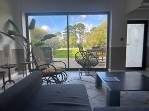 Moderni sisustus, jossa on sohva, kaksi tuolia, pieni pöytä ja lasiovesta avautuva näkymä ulkotilalle, jossa on patio.