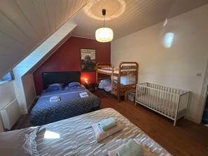 Makuuhuoneessa on kerrossänky, vauvansänky, kuviollinen päiväpeite, juliste seinällä ja kalteva katto.