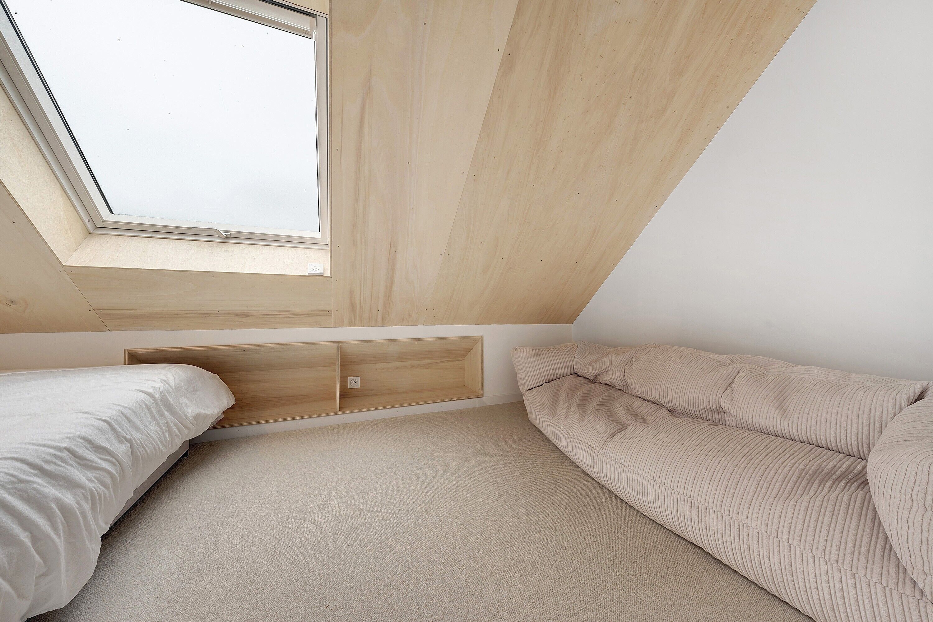 Une chambre dotée d’une lucarne, d’un lit, d’un canapé et d’un meuble de rangement intégré.
