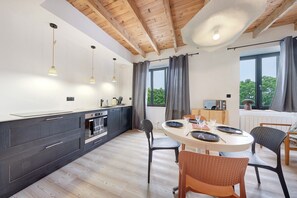 Una cucina moderna con travi in legno, luci a sospensione, un'area pranzo con sedie e un'ampia finestra.