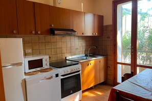 Cozinha com armários de madeira, micro-ondas, fogão, forno, pia e janela com vista para o verde.