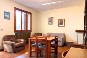 Uma sala de estar com sofá, mesa de jantar com cadeiras, poltrona marrom e duas imagens emolduradas na parede.