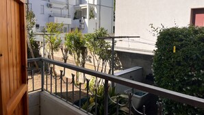 Uma varanda com vista para um edifício branco, uma porta de madeira e um corrimão de metal.