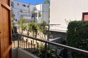 Un balcone con vista su un edificio bianco, una porta in legno e una ringhiera in metallo.