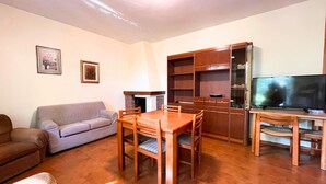 Uma sala de estar com sofá, mesa de jantar e cadeiras, televisão e um armário de madeira.