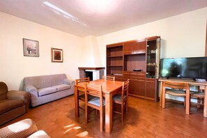 Uma sala de estar com sofá, mesa de jantar e cadeiras, televisão e um armário de madeira.