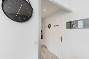 Ein Korridor mit einer Uhr, einer Tür mit der Aufschrift 'Salle d'Od' und einem Schwarzes Brett mit Aushängen.