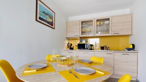 A dining area with a round table, yellow chairs, and a kitchen in the background. - Sea View in the Heart of Morgat (Crozon)