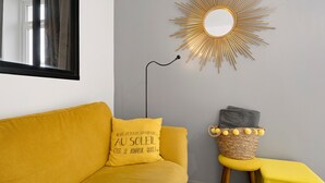 A room with a yellow sofa, a small stool, a wall-mounted mirror, and a sunburst light fixture. - Sea View in the Heart of Morgat (Crozon)