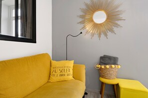 Ein Zimmer mit einem gelben Sofa, einem kleinen Hocker, einem wandmontierten Spiegel und einer sternförmigen Lampenleuchte.