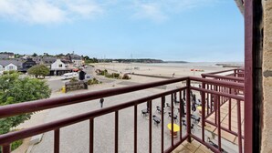 A balcony with a view of a beach, a paved area with tables and chairs, and buildings in the background. - Sea View in the Heart of Morgat (Crozon)