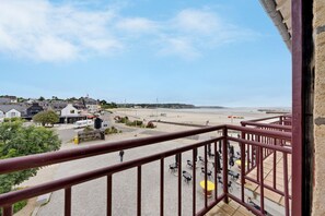 A balcony with a view of a beach, a paved area with tables and chairs, and buildings in the background. - Sea View in the Heart of Morgat (Crozon)