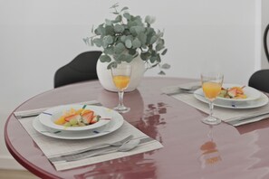 A round table with two plates of fruit and two glasses of orange juice, a white vase with green foliage, and a black chair. - Bright Loft | Fully Equipped | Smart TV | AC | Sleeps 2 (Torrefiel)