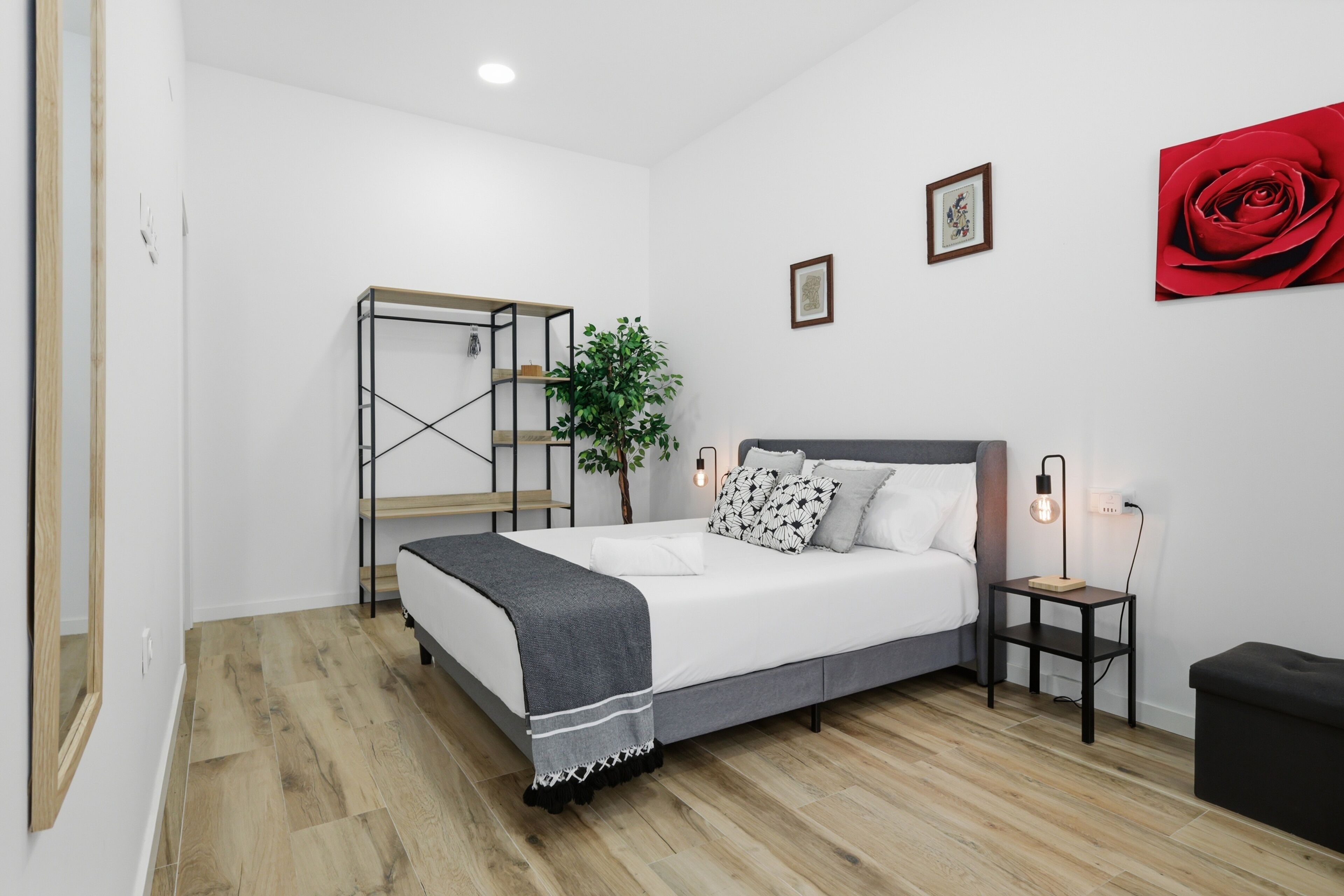 A bedroom with a bed, bedside tables, a plant, and a red rose painting.