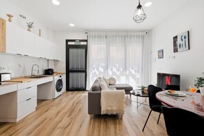 A modern kitchen with a washing machine, a dining area with a table and chairs, and a living area with a sofa.