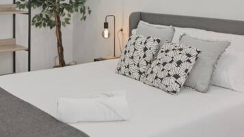 Una cama bien hecha con almohadas estampadas, una planta en la mesita de noche y un aplique de pared.