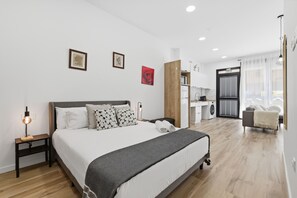 A modern hotel room with a large bed, a desk, a washing machine, and a view of the outside. - Bright Loft | Fully Equipped | Smart TV | AC | Sleeps 2 (Torrefiel)