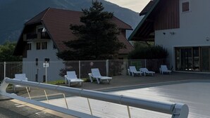 Un hotel con vistas a la montaña, zona de piscina con tumbonas y un patio vallado.