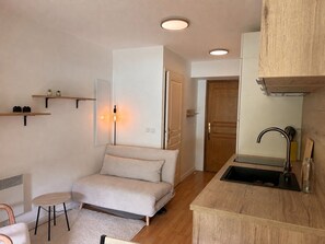 A compact living space with a kitchenette, a sofa, a small round table, and a door leading to another room. - 🏡 Le Birdie – Studio with Balcony Between Lake and Mountains (Giez)