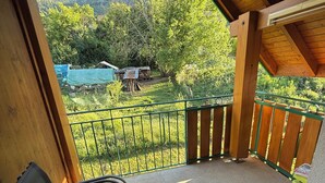 Un espacio al aire libre cubierto con vistas a un paisaje montañoso, una valla de metal verde y una pila de leña.