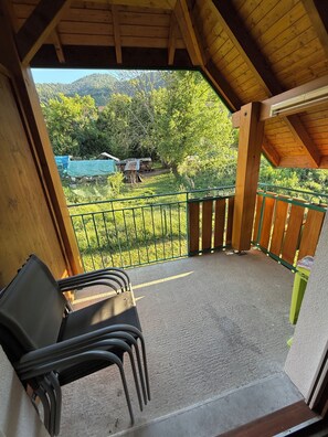 A covered outdoor area with a view of a mountainous landscape, a green metal fence, and a stack of firewood. - 🏡 Le Birdie – Studio with Balcony Between Lake and Mountains (Giez)