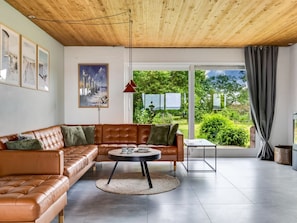Ein modernes Wohnzimmer mit einer Ledersofa, einem runden Couchtisch und Blick auf einen üppigen Garten durch große Fenster.