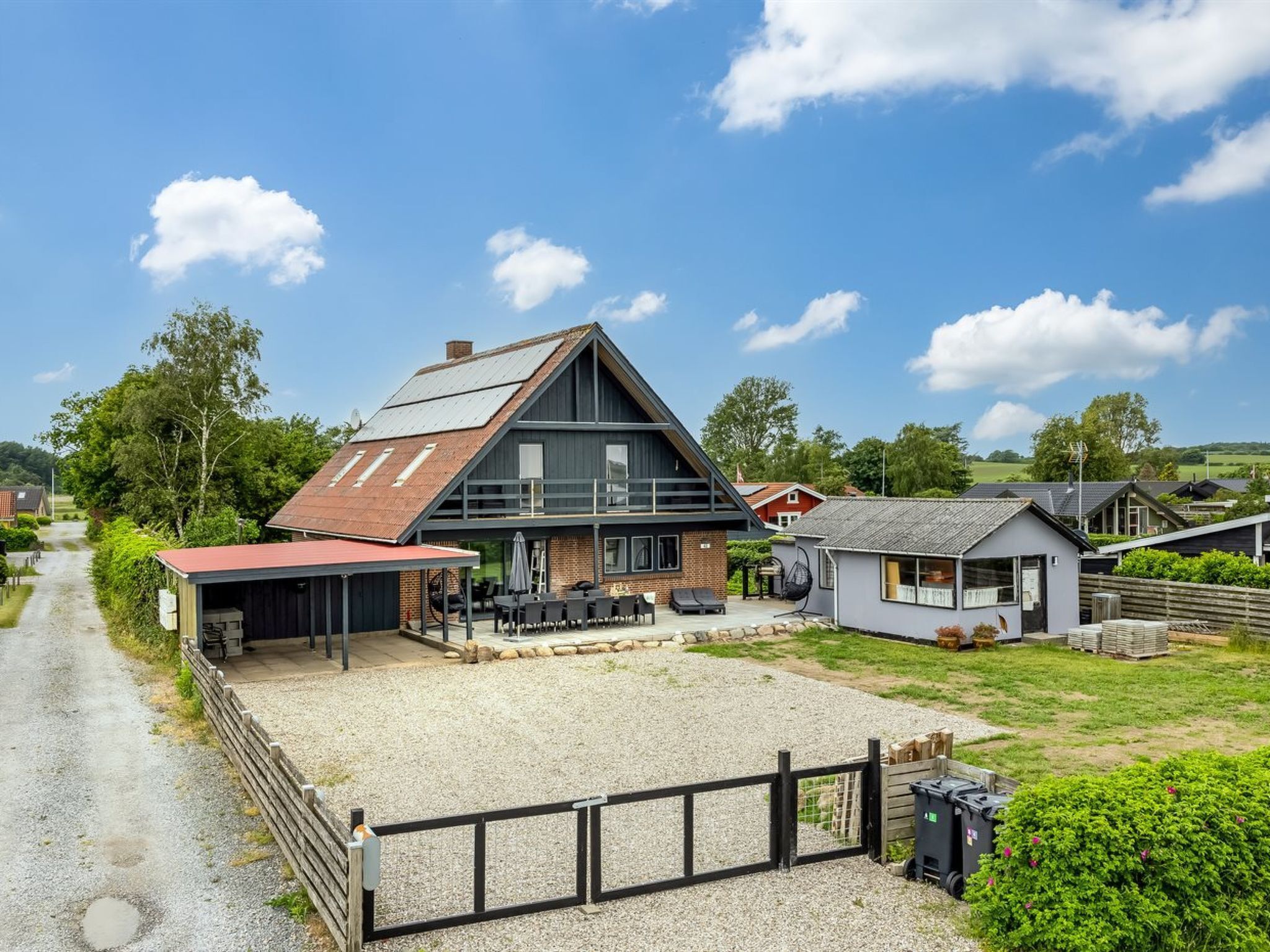 Ein modernes, zweistöckiges Haus mit Kiesauffahrt, Sitzbereich im Freien und einem umzäunten Garten.