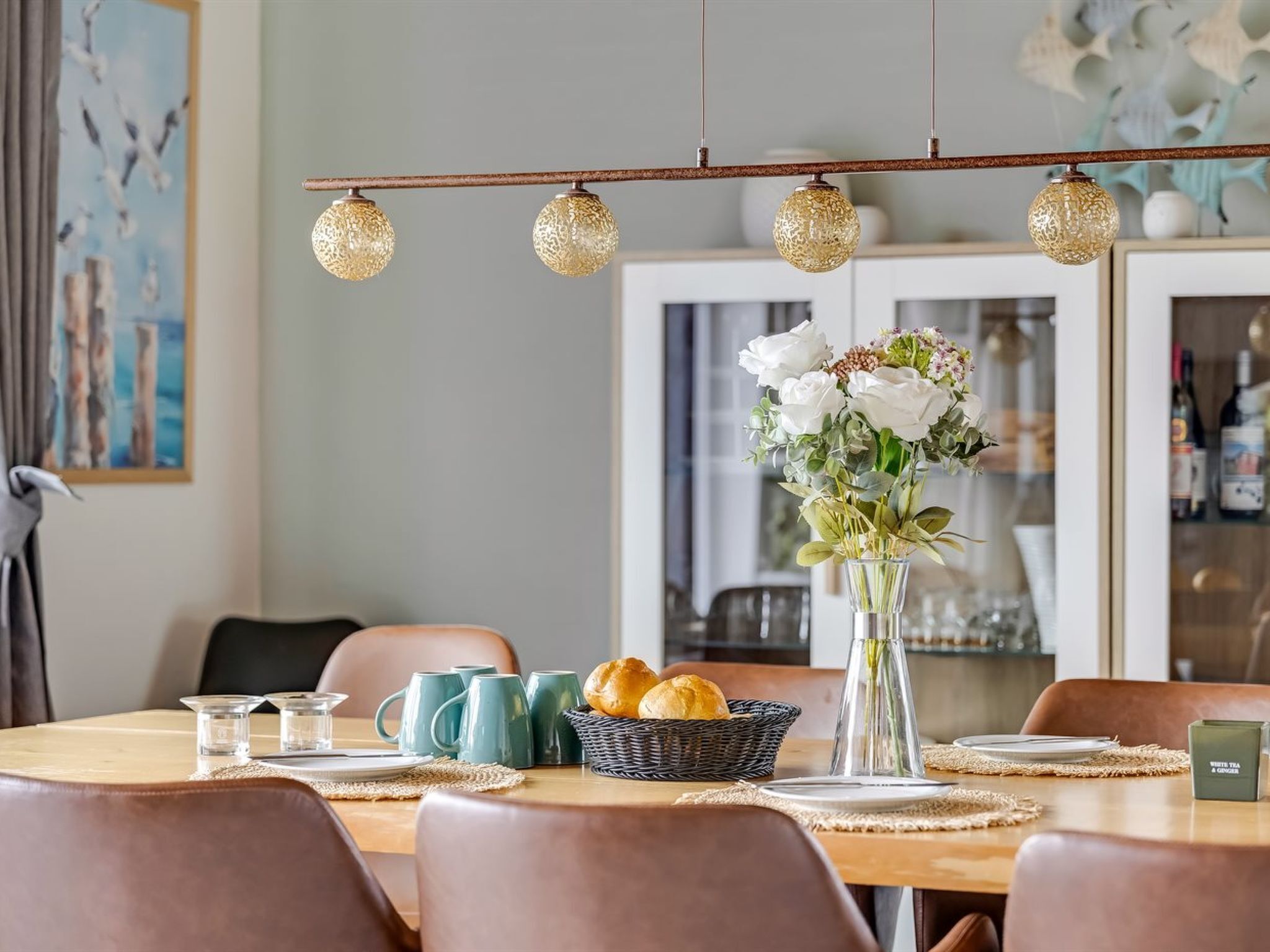 A dining area with a table set for four, a vase of flowers, and a hanging light fixture.