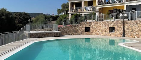 A clear swimming pool with a stone wall and a building with balconies in the background.