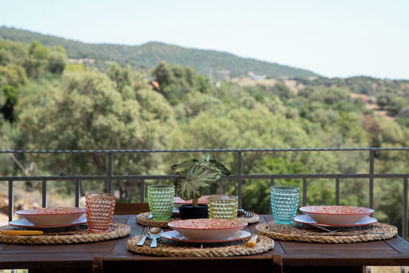 Ein Tisch ist mit Tellern, Schüsseln und Gläsern auf einem Balkon mit Blick auf eine Berglandschaft gedeckt.