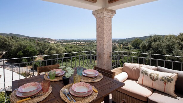 A balcony with a table set for dining, a cushioned seating area, and a view of a green landscape. - Casa Luna e Sole by Wonderful Italy (Maiorca)