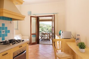 Een keuken met een gasfornuis, oven en een eethoek met een tafel en stoelen.