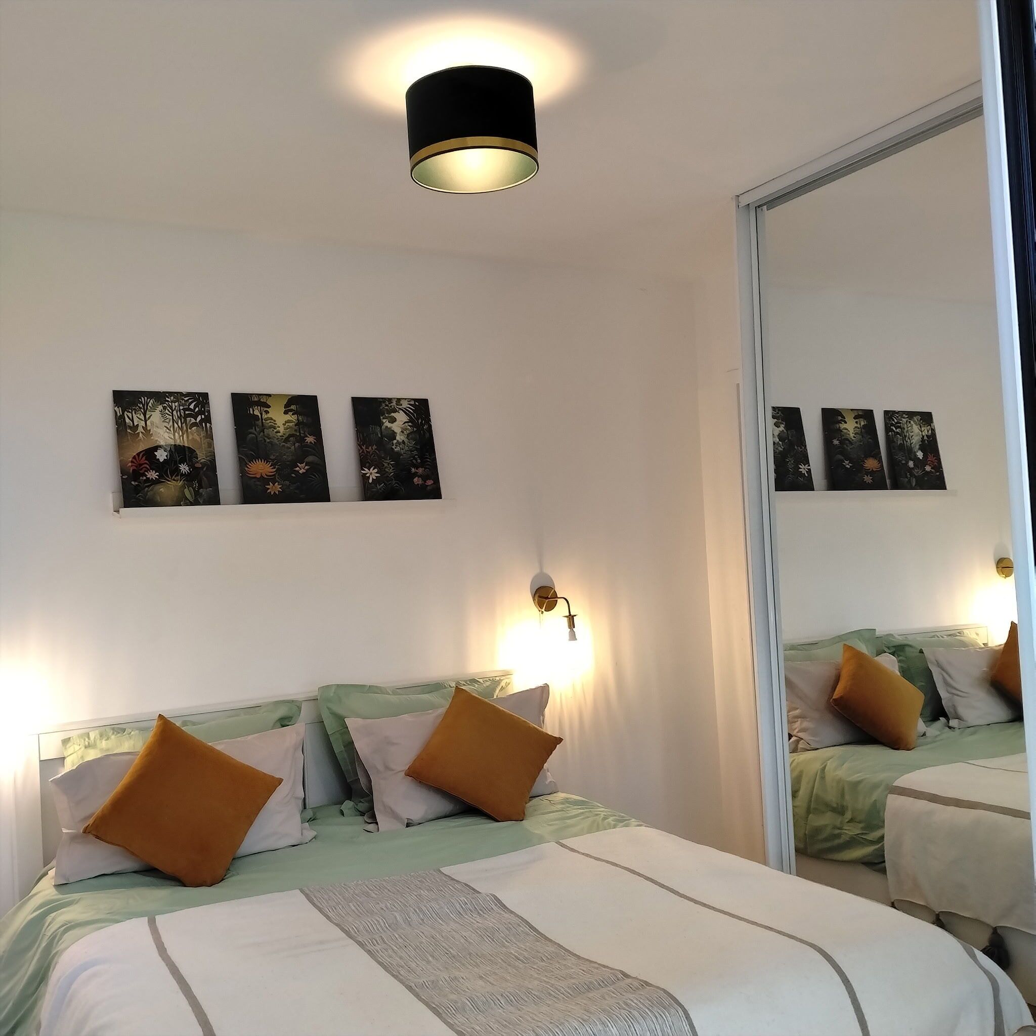Une chambre d’hôtel avec un lit, une lampe fixée au mur et trois tableaux.