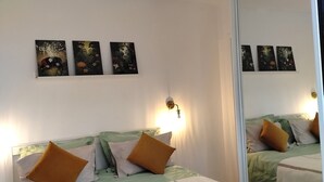 Una habitación de hotel con una cama, una lámpara fijada a la pared y tres cuadros.