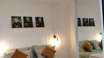 Une chambre d’hôtel avec un lit, une lampe fixée au mur et trois tableaux.