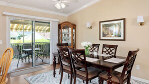 A dining room with a table, chairs, a ceiling fan, a large window, and a framed picture on the wall. - Twisted Palms - 3/2 Dog Friendly w/ Golf Cart in The Village of Amelia (Amelia, The Villages)