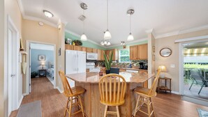 A kitchen with a central island, wooden chairs, pendant lights, and a view of the outdoors. - Twisted Palms - 3/2 Dog Friendly w/ Golf Cart in The Village of Amelia (Amelia, The Villages)