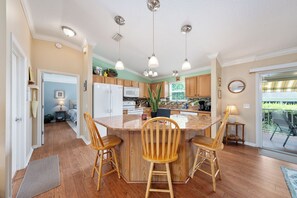 Una cocina con isla central, sillas de madera, luces colgantes y vistas al exterior.