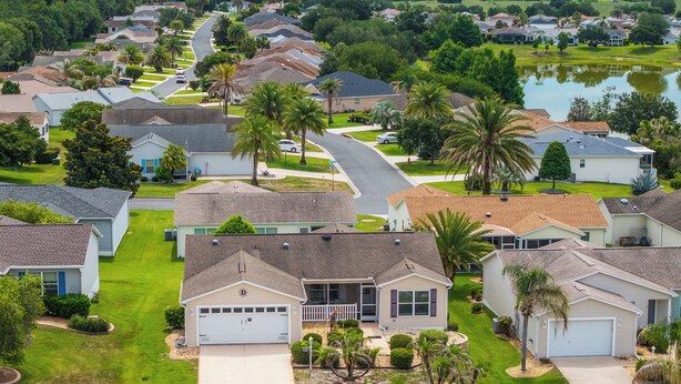 A residential area with single-family homes, a curved road, and a body of water in the background. - Twisted Palms - 3/2 Dog Friendly w/ Golf Cart in The Village of Amelia (Amelia, The Villages)