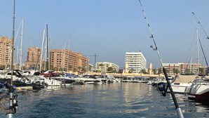 Una marina con barcos, cielo despejado y edificios al fondo.