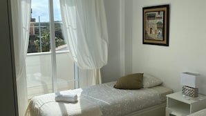 Un dormitorio con cama, mesita de noche, cortinas en la ventana y un cuadro en la pared.