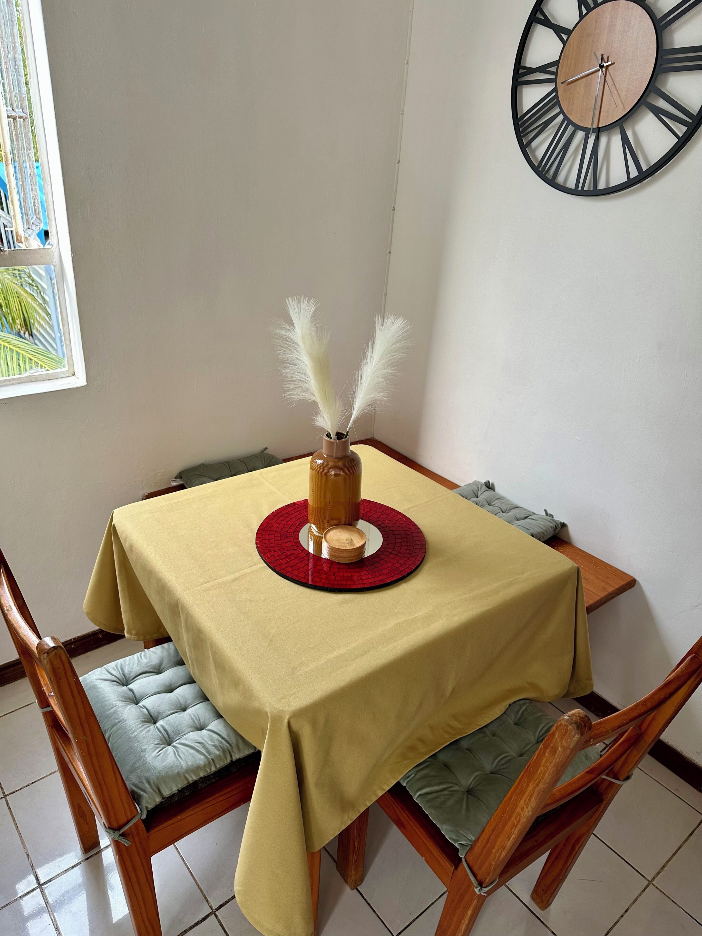 A dining table with a yellow tablecloth, a red placemat, and a vase with white feathers.