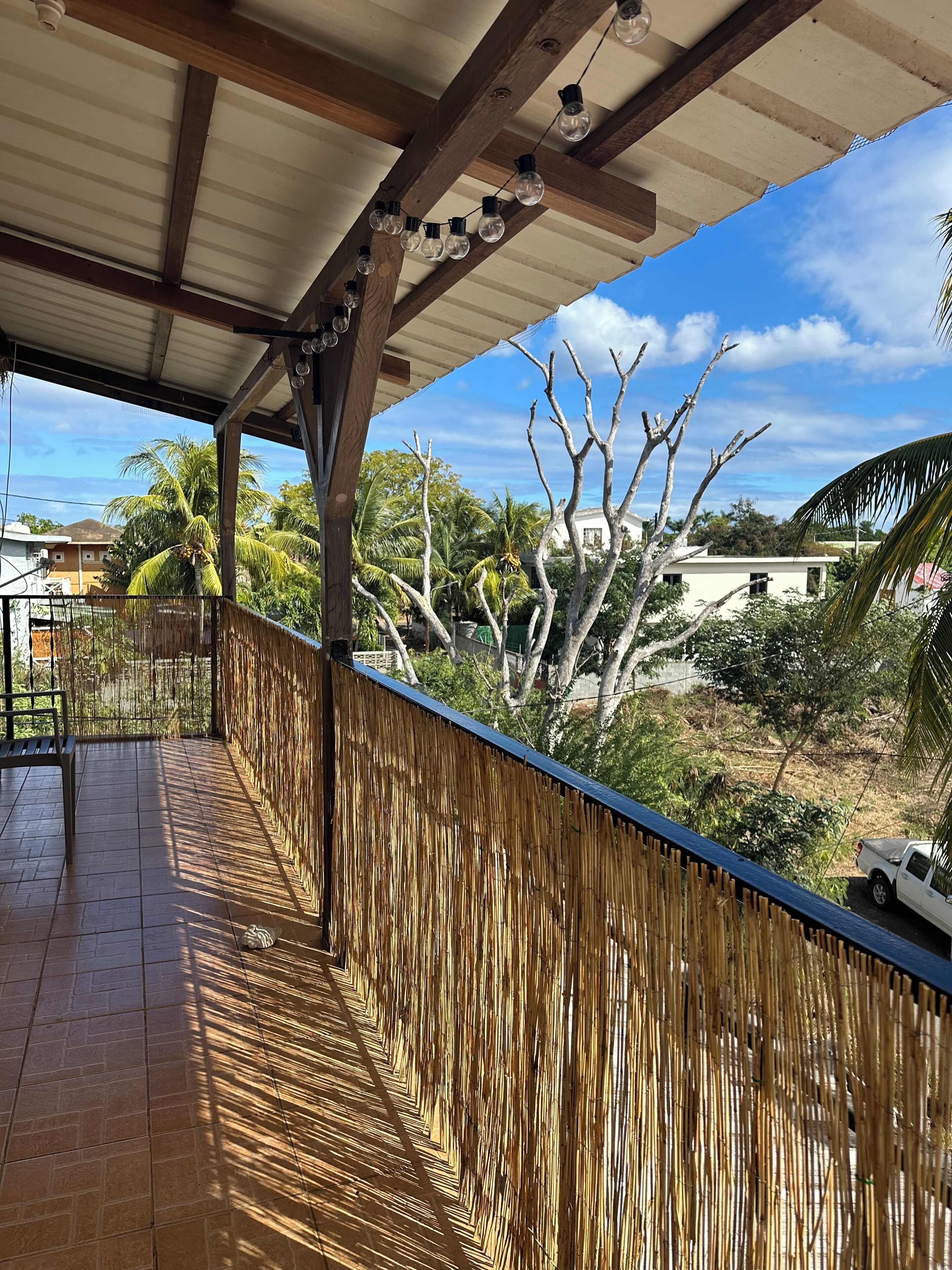 A covered outdoor area with a bamboo fence, a bench, and a view of the surrounding landscape.