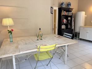 Ein Esstisch mit einer Vase und Weingläsern, ein gelber Stuhl, ein Bücherregal und ein weißes Schrank.